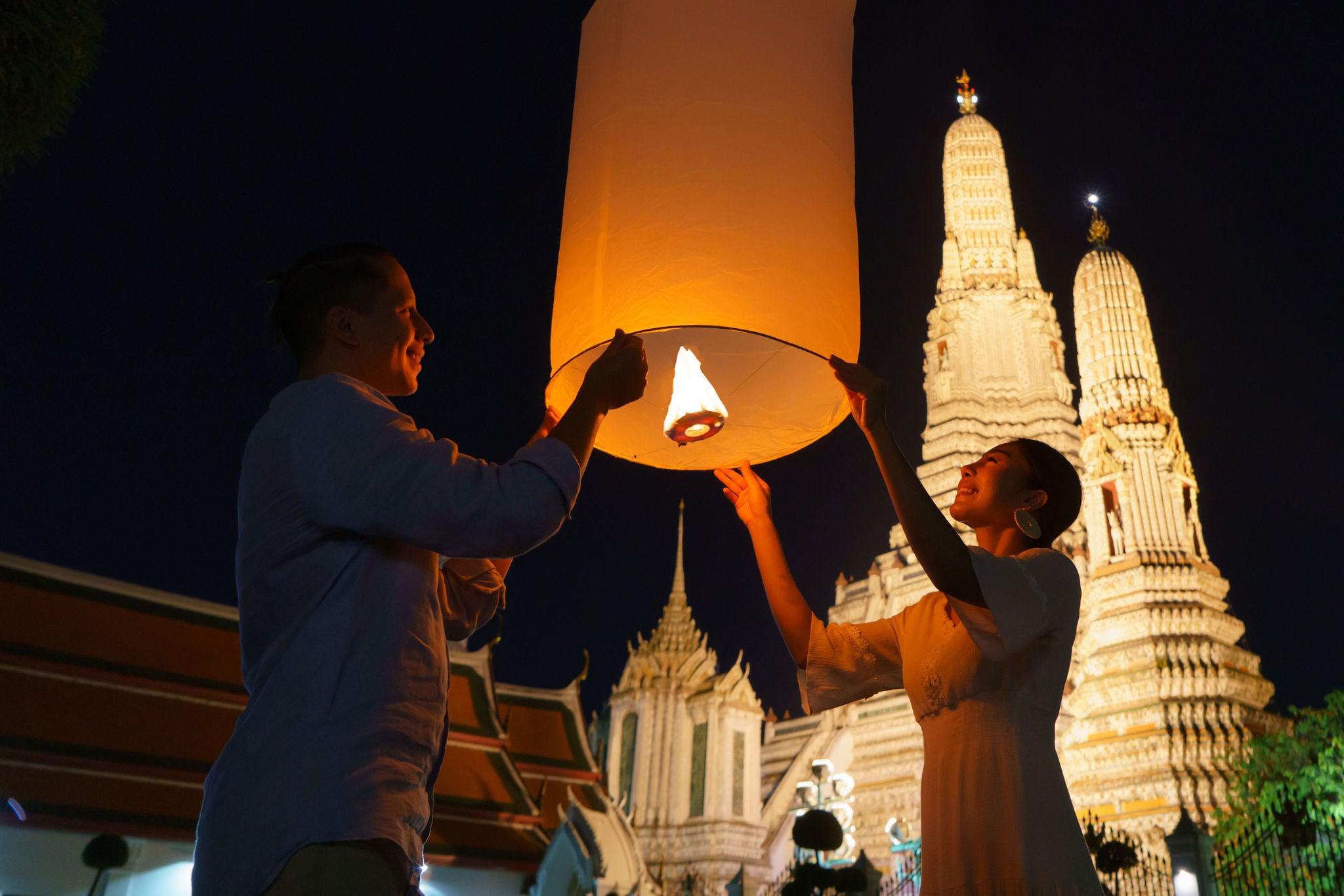 Mixed race romantic lover couple in Wat arun in night time and floating lamp in Yi Peng festival under Loy Krathong day, Bangkok city ,Thailand
