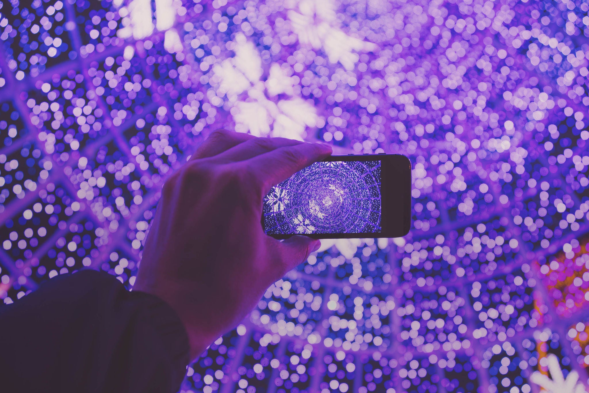 Original picture of a man taking picture with smartphone inside a big Christmas tree in Andorra la Vella for the winter festivities.